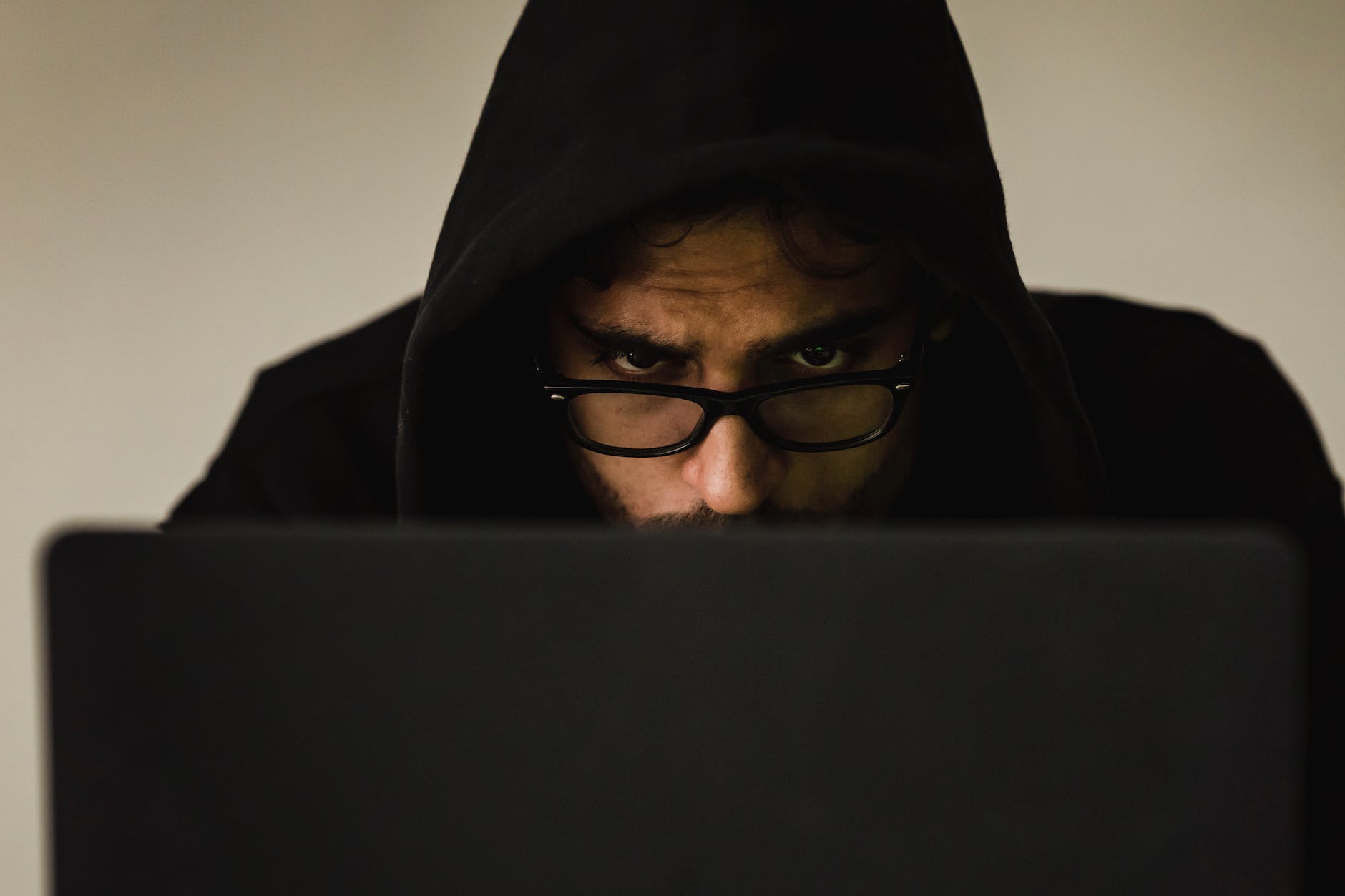 crop focused hacker in hood using laptop