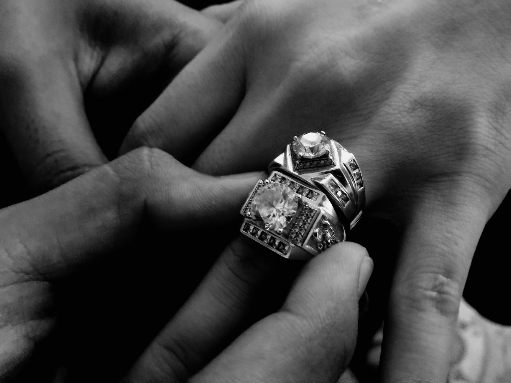 grayscale photo of person wearing two diamond encrusted rings